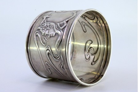  Argola de guardanapo com relevos femininos e laços envolvidos.